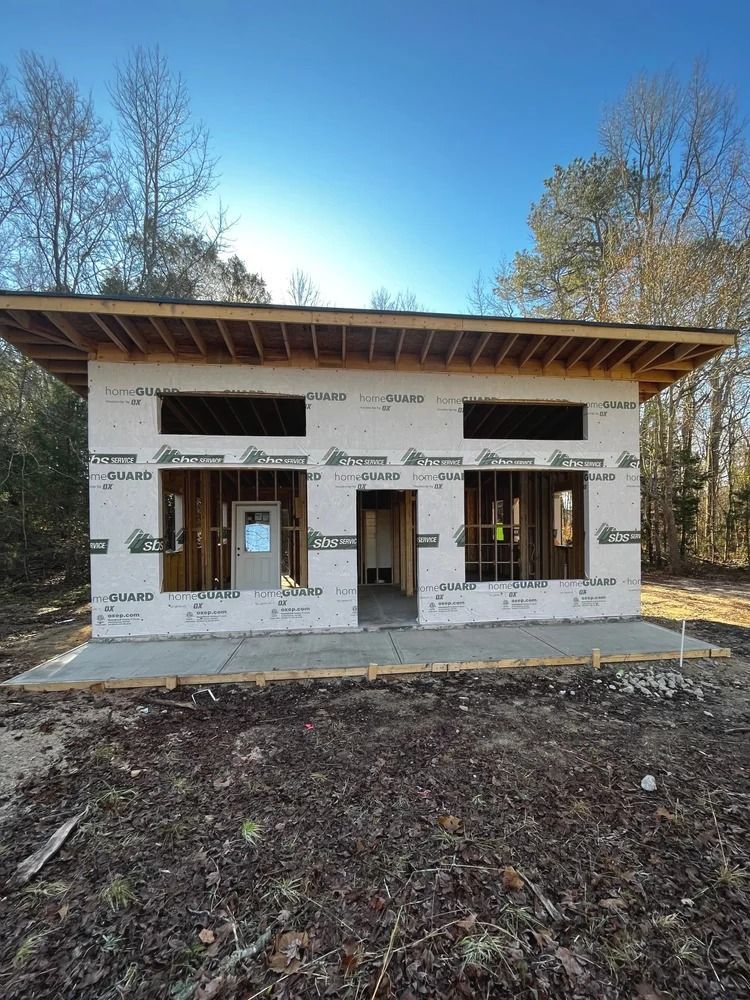Partially built two-story house with wood framing and white house wrap under a blue sky