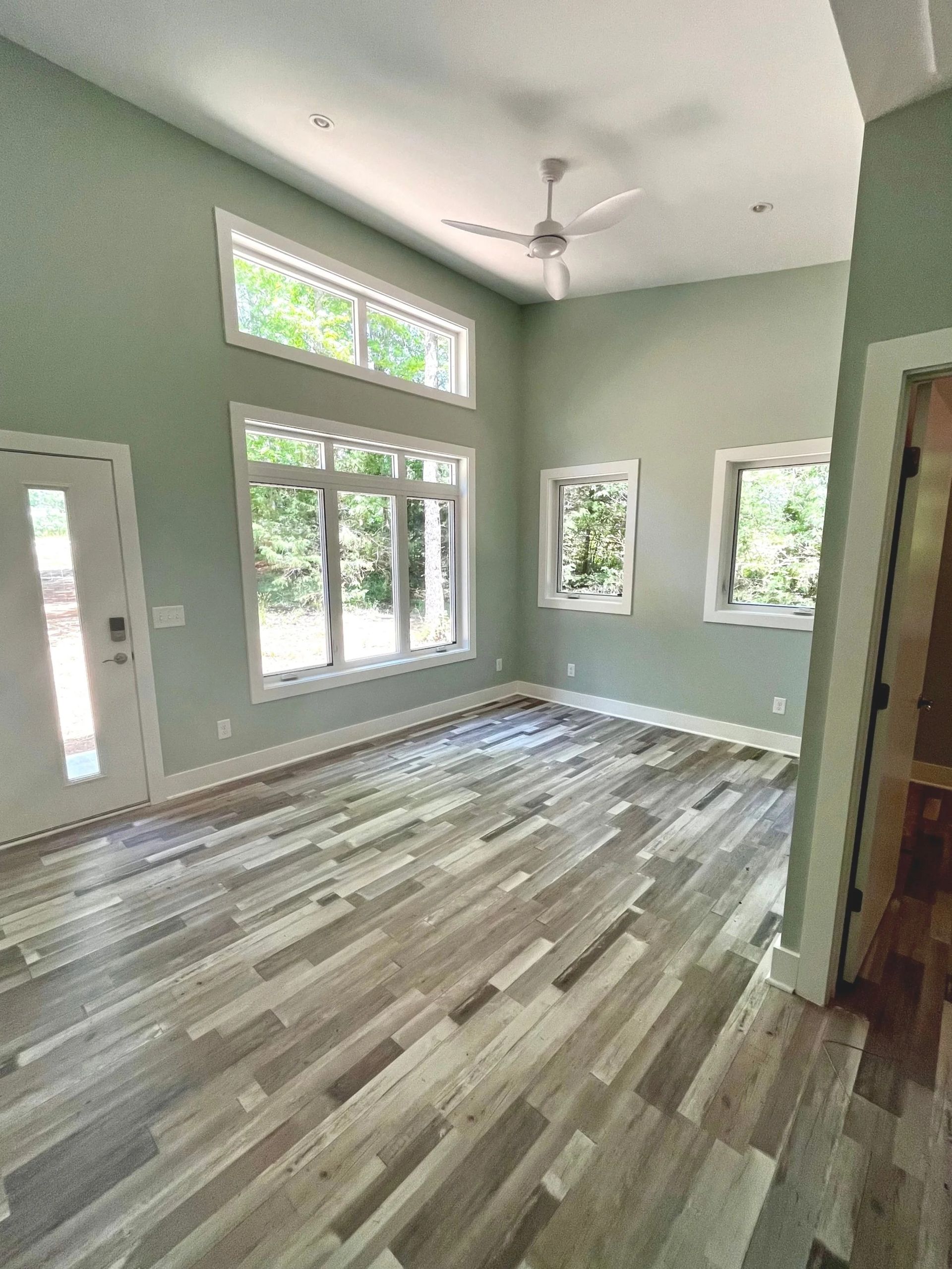 Empty living room with tall windows, gray walls, and wood-look flooring.