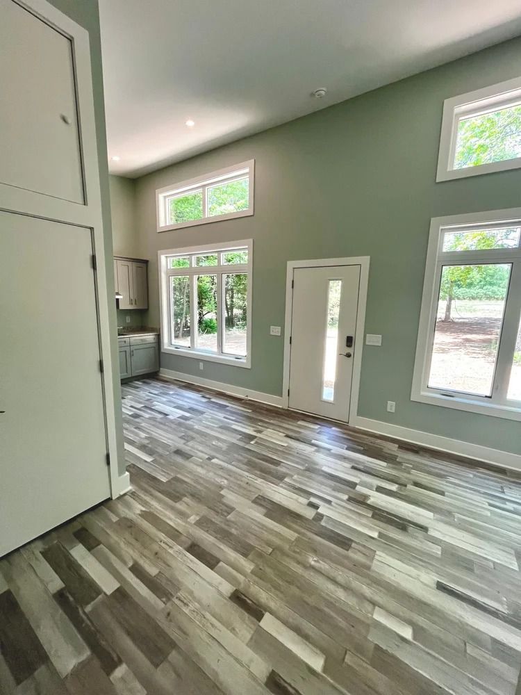 Empty modern room with high windows, sage green walls, and wood-look floors