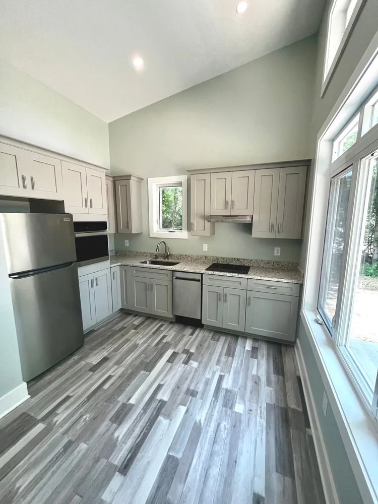 Bright modern kitchen with stainless appliances, gray cabinets, and large windows.