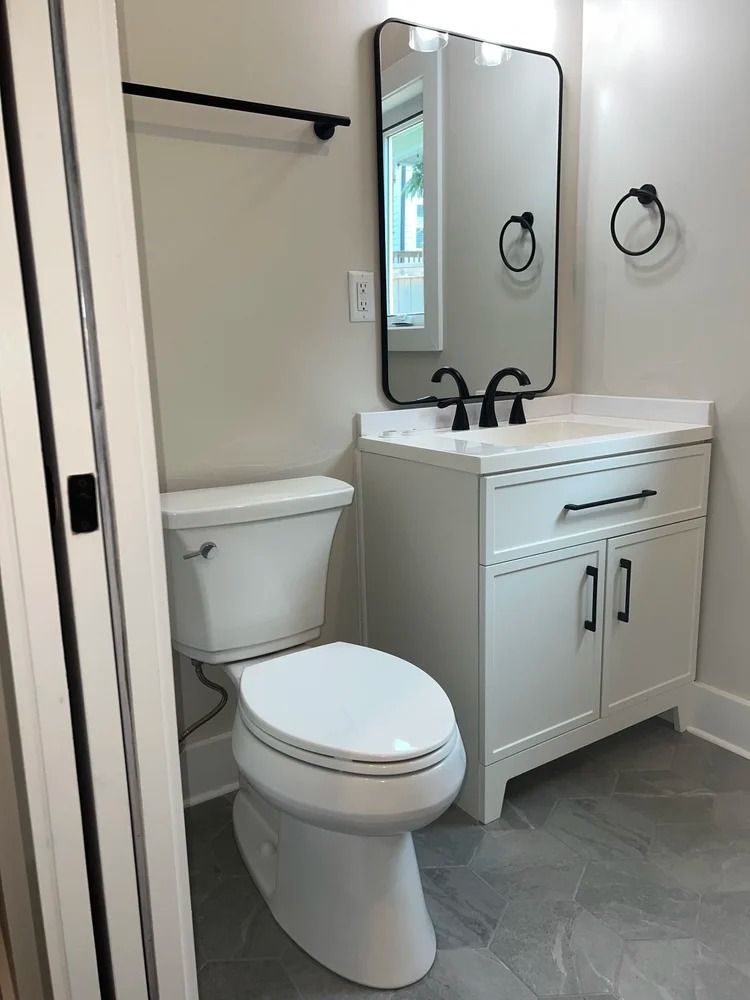 Compact bathroom with white toilet, vanity, mirror, towel bar, and gray tile floor.