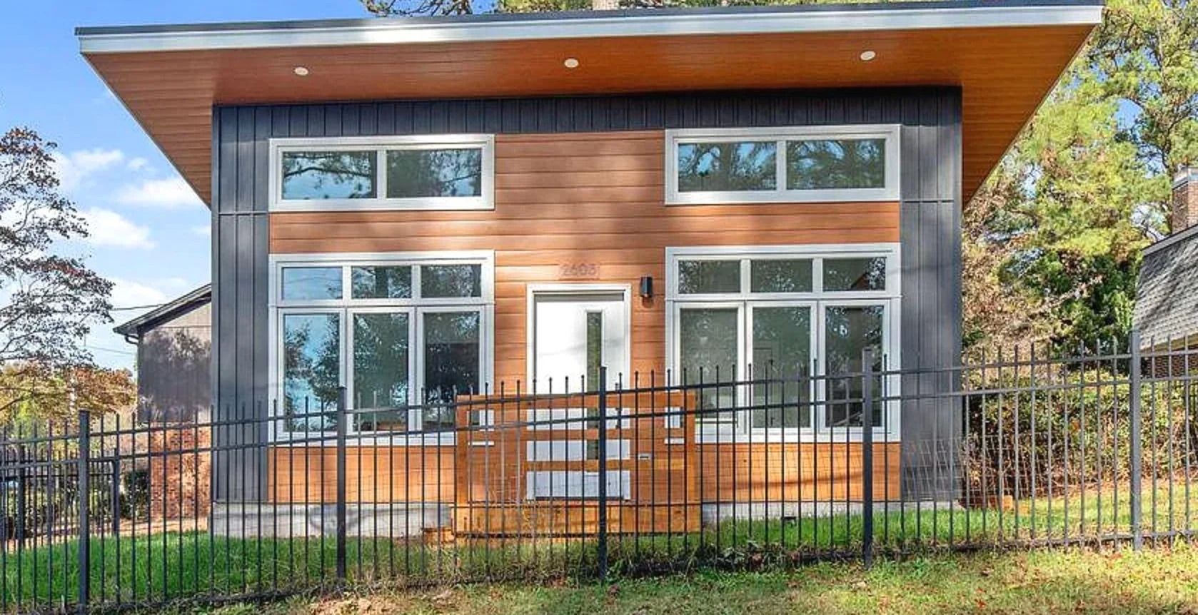 Modern wood-sided house with large windows and a fenced front yard
