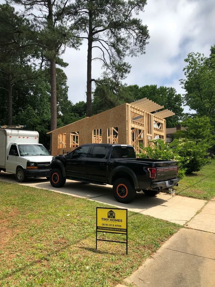 New home under construction beside parked truck and van, with a yard sign in front