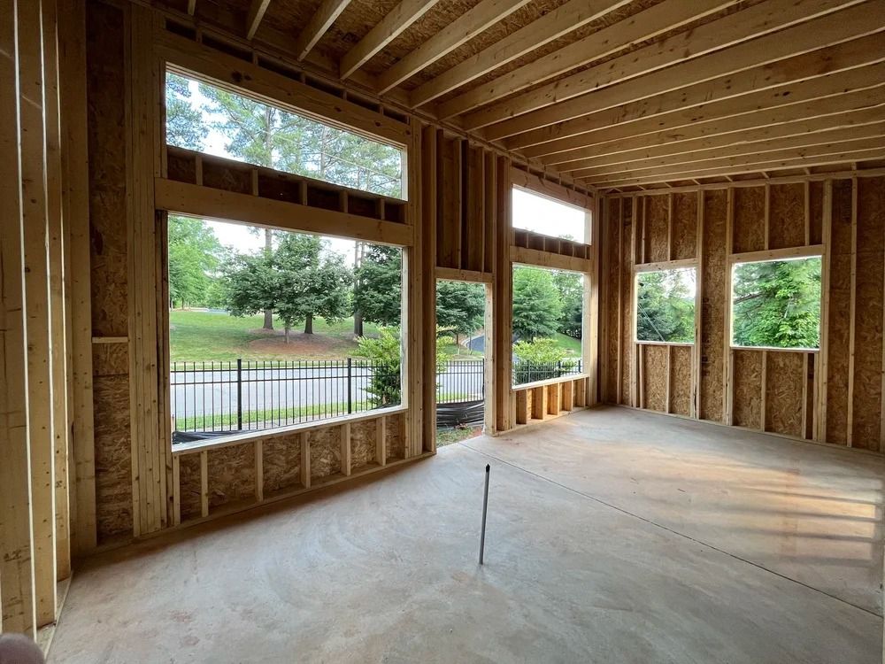 Unfinished wood-framed room interior with large windows overlooking a river and trees