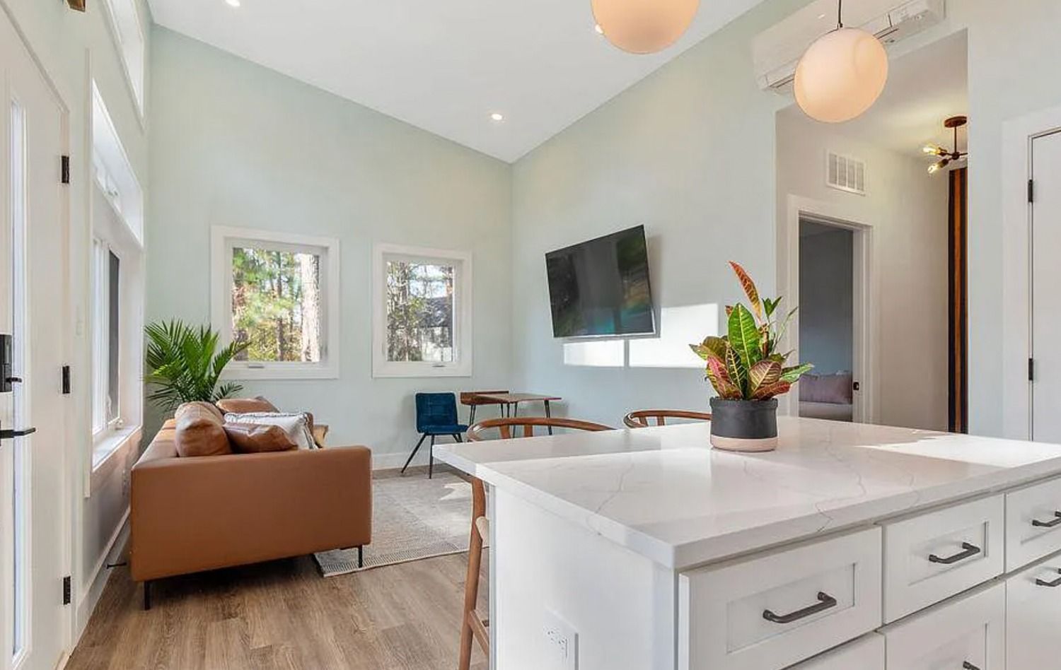 Bright modern living room with a brown sofa, wall-mounted TV, and white kitchen island in the foreground