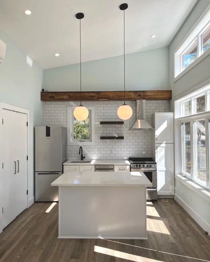 Bright modern kitchen with white island, pendant lights, wood beam, and large windows