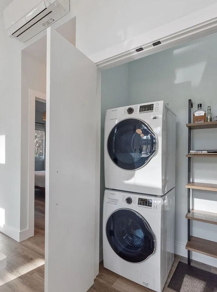 Stacked washer and dryer in a bright laundry nook beside a shelving unit