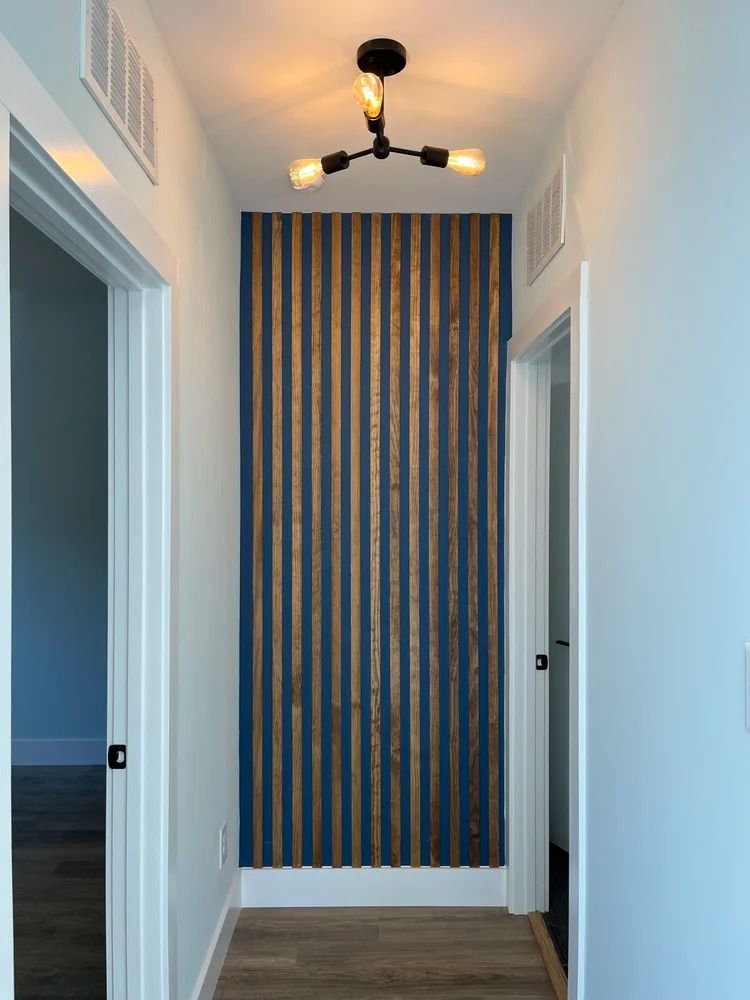 Narrow hallway with blue-and-white striped accent wall, wood floor, and modern ceiling light fixtures.