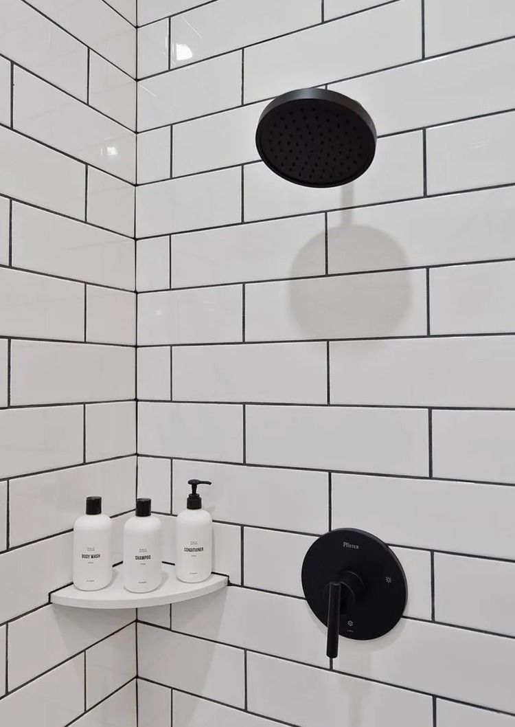Modern shower with white subway tile, black fixtures, shelf of toiletries, and a black showerhead.