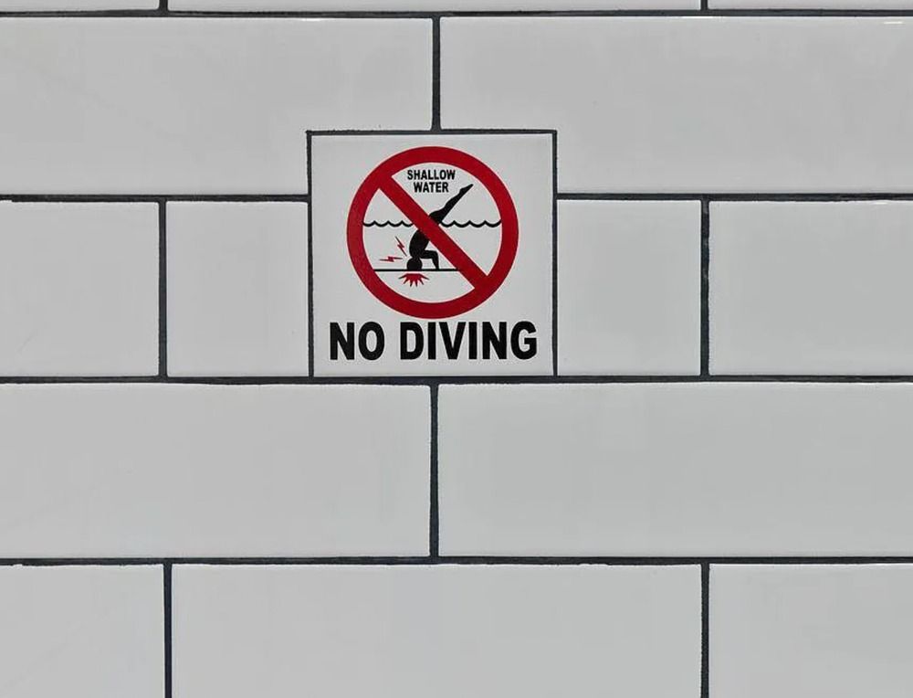 No diving sign on a tiled wall, with a red circle-and-slash over a diver symbol.