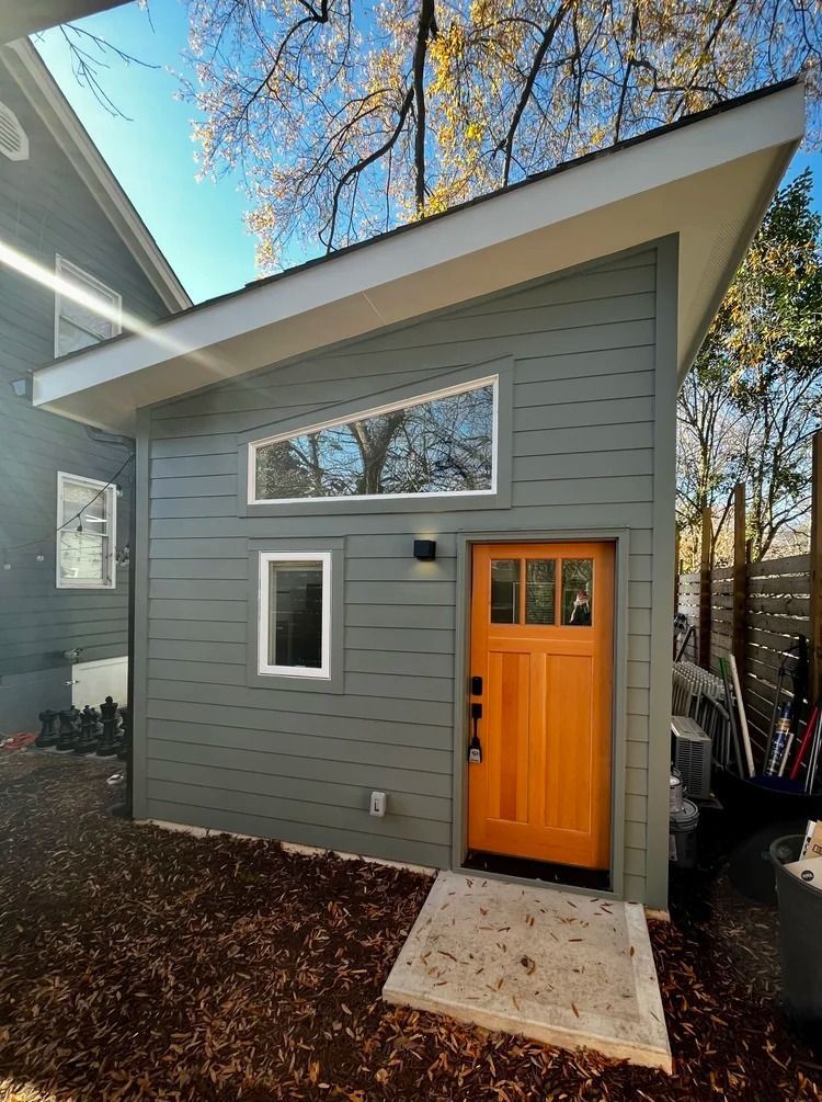 Modern gray house exterior with bright orange front door and white concrete step.