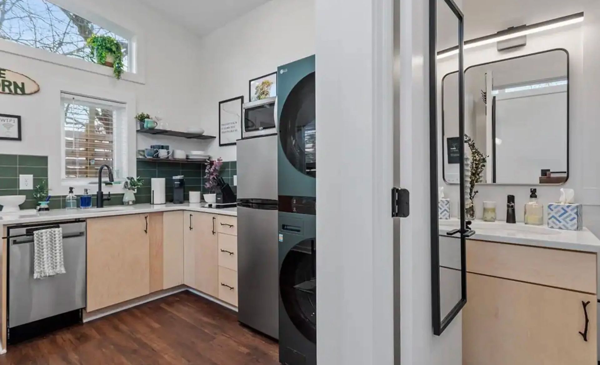 Modern kitchen with light wood cabinets, stainless appliances, and a view into a bathroom vanity area