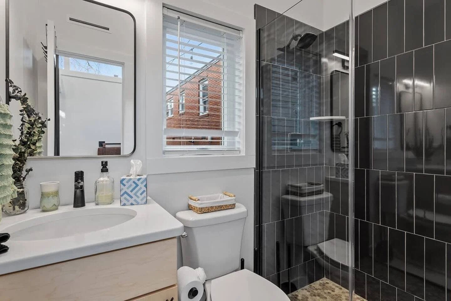 Modern bathroom with white vanity, window, and glass-enclosed shower with dark tile.