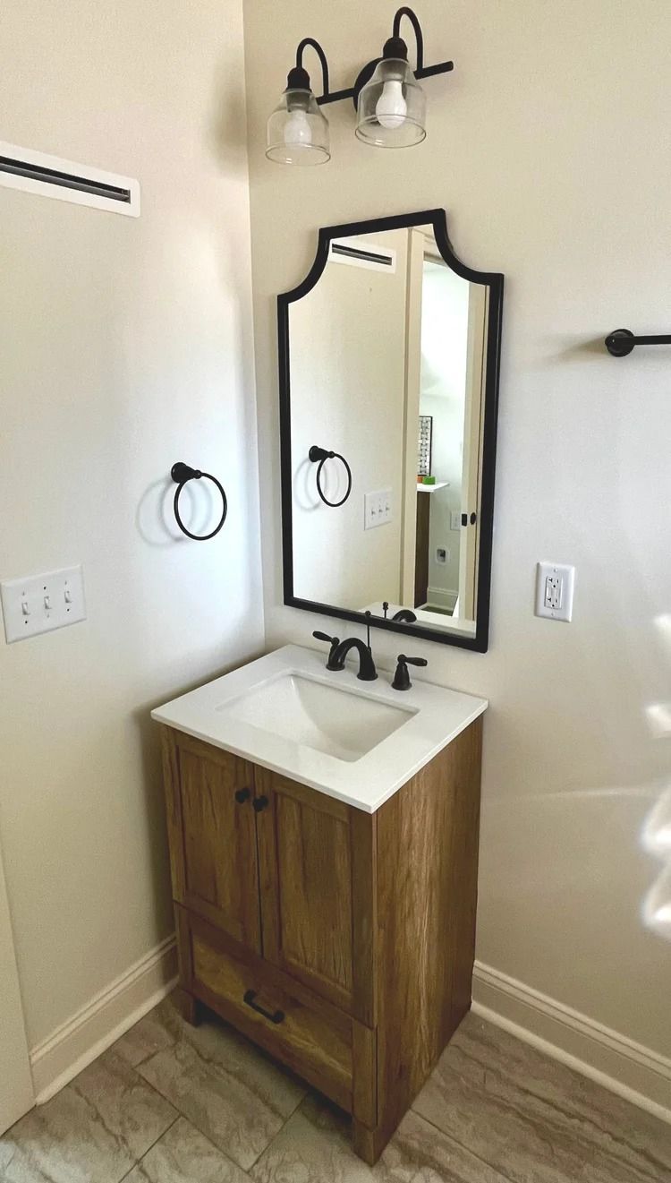 Small bathroom vanity with wood cabinet, white sink, black faucet, mirror, and wall light fixture.
