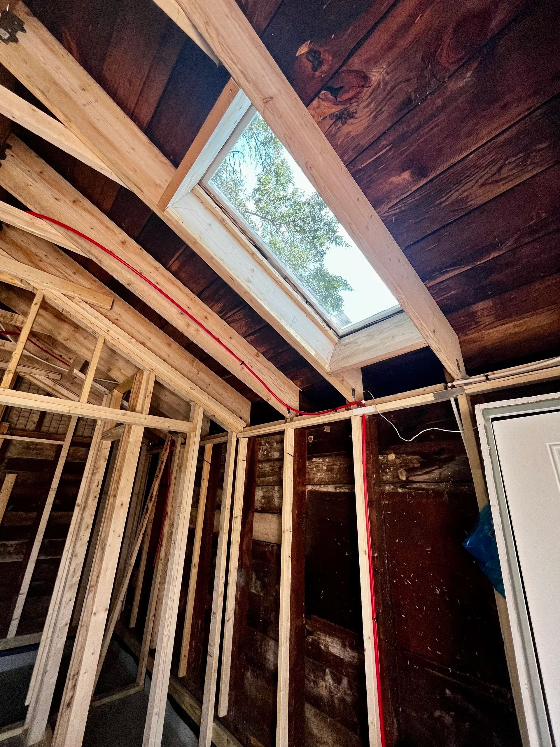 Interior under renovation with exposed framing, dark wood walls, and a skylight opening above