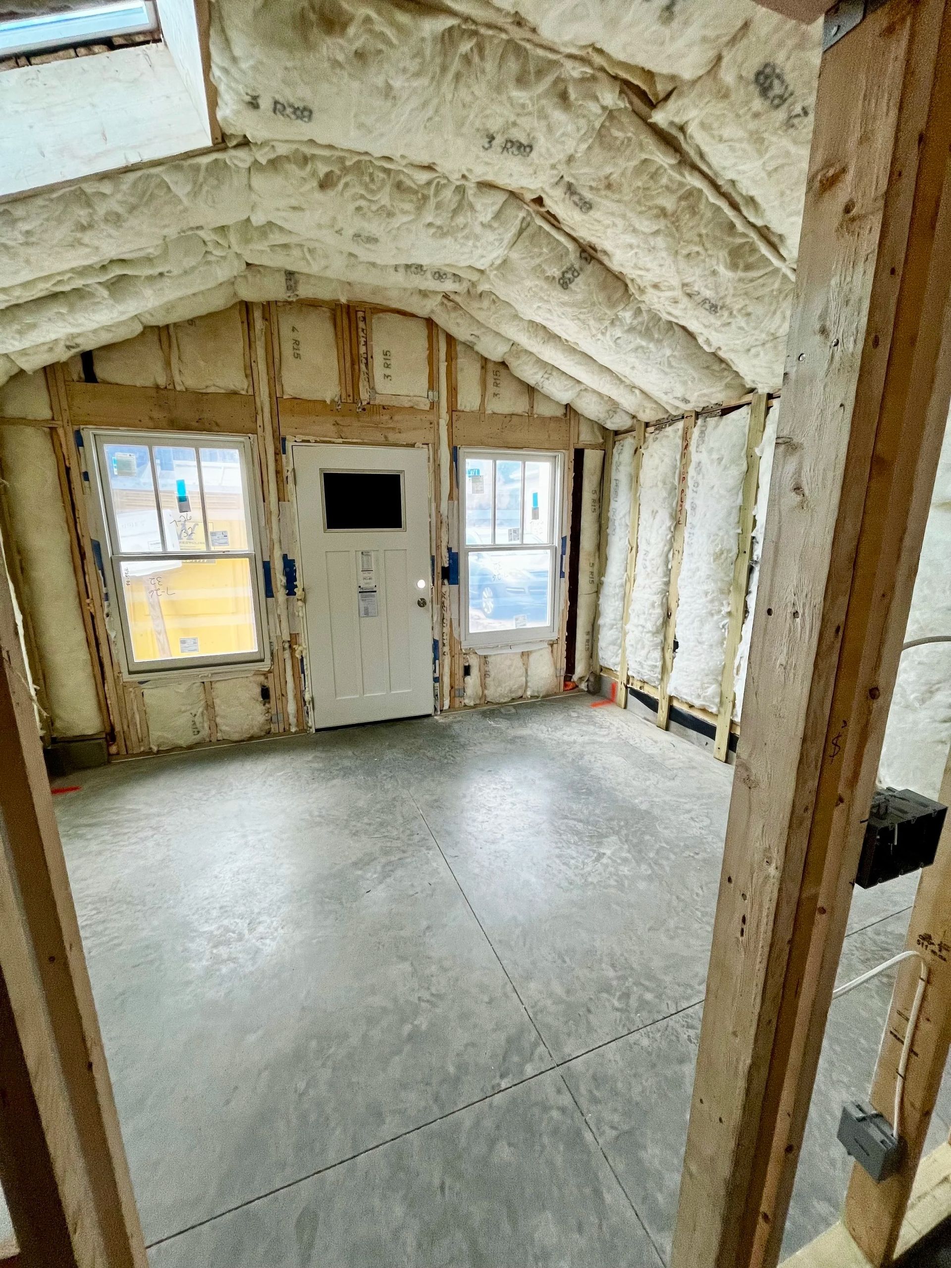 Unfinished room with spray foam insulation, exposed studs, and a white door with windows.