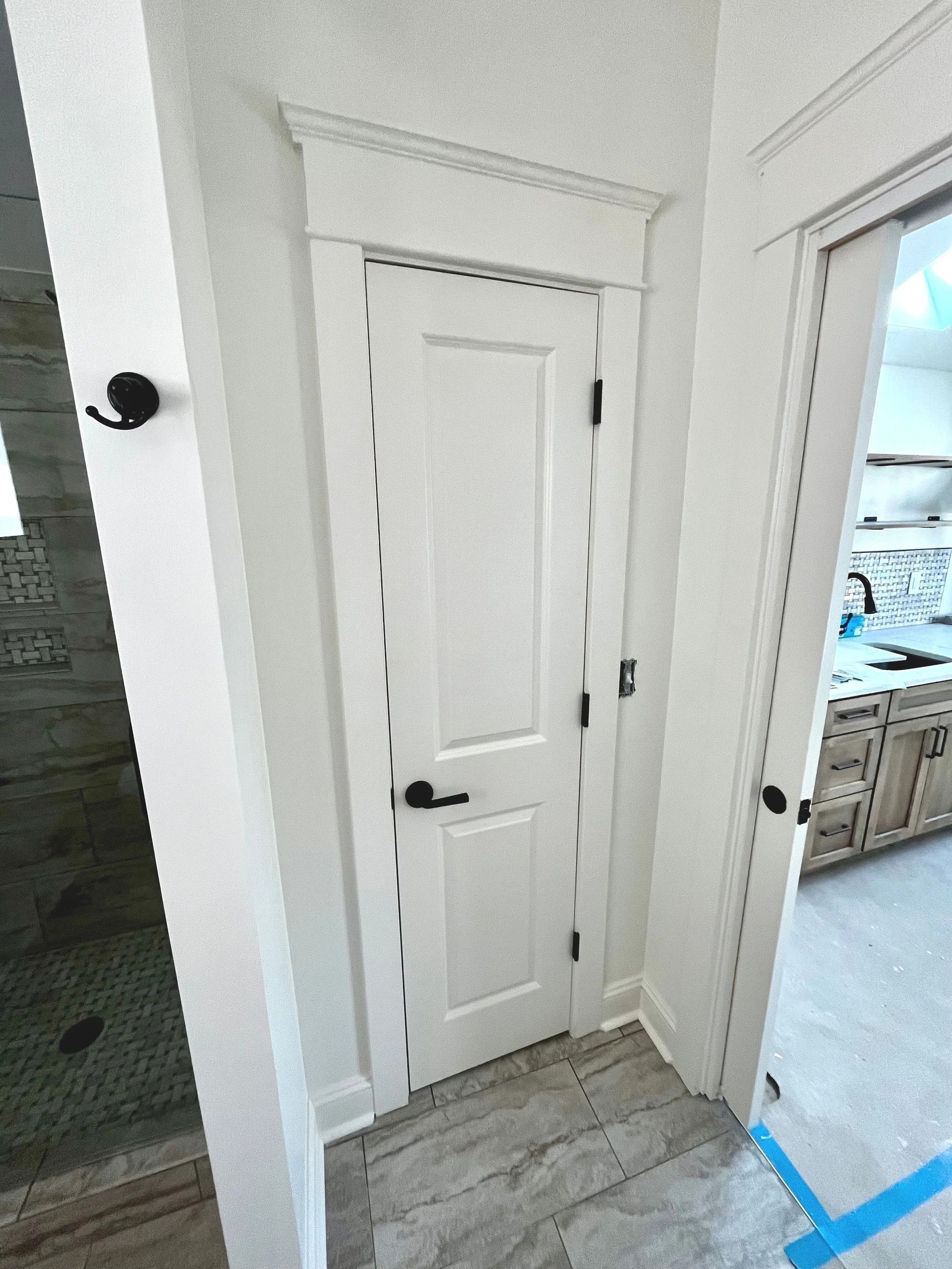 Narrow white hallway with closet door, gray tile floor, and open doorway to a kitchen with blue painter’s tape