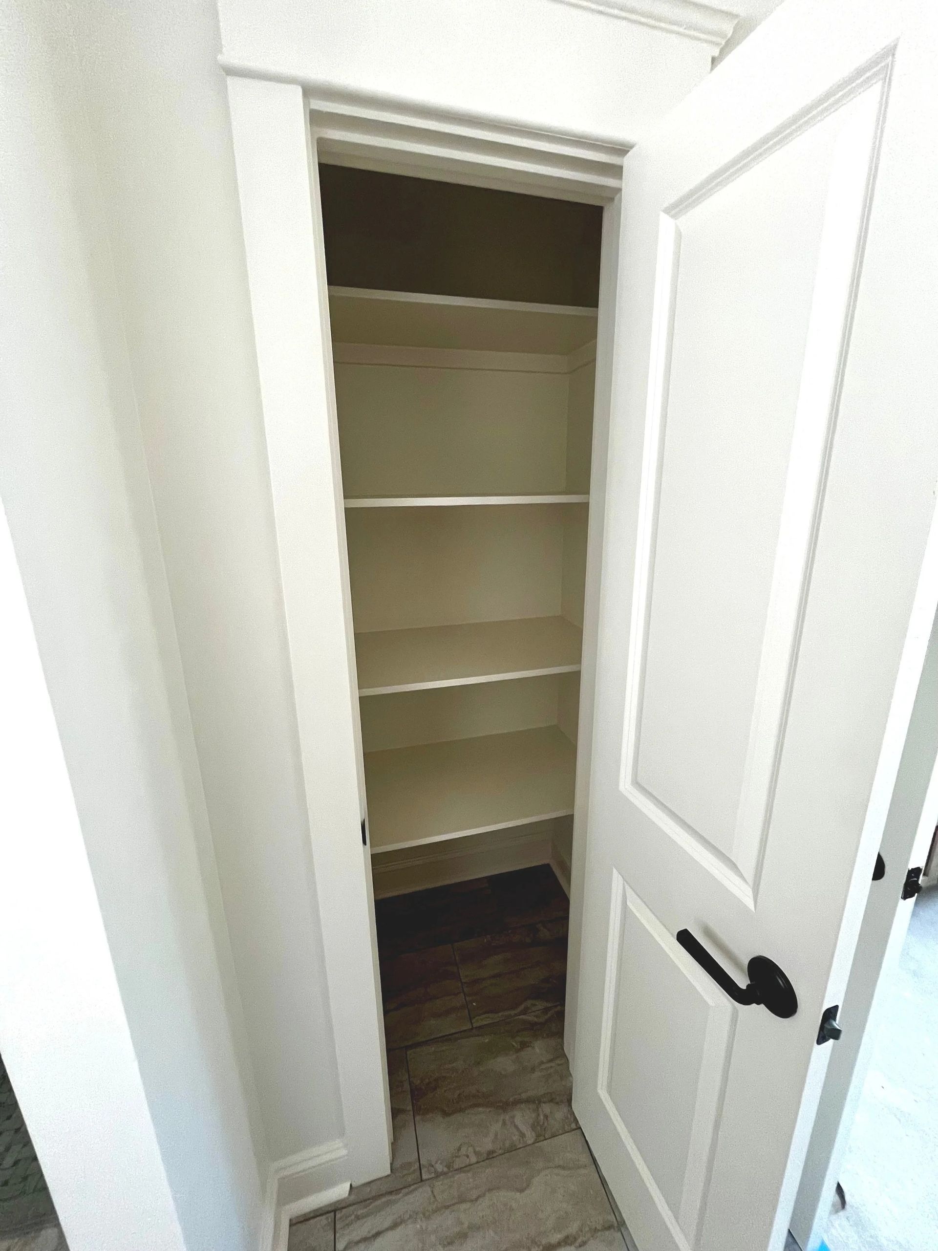 Open white closet door revealing empty shelves inside a small hallway closet.