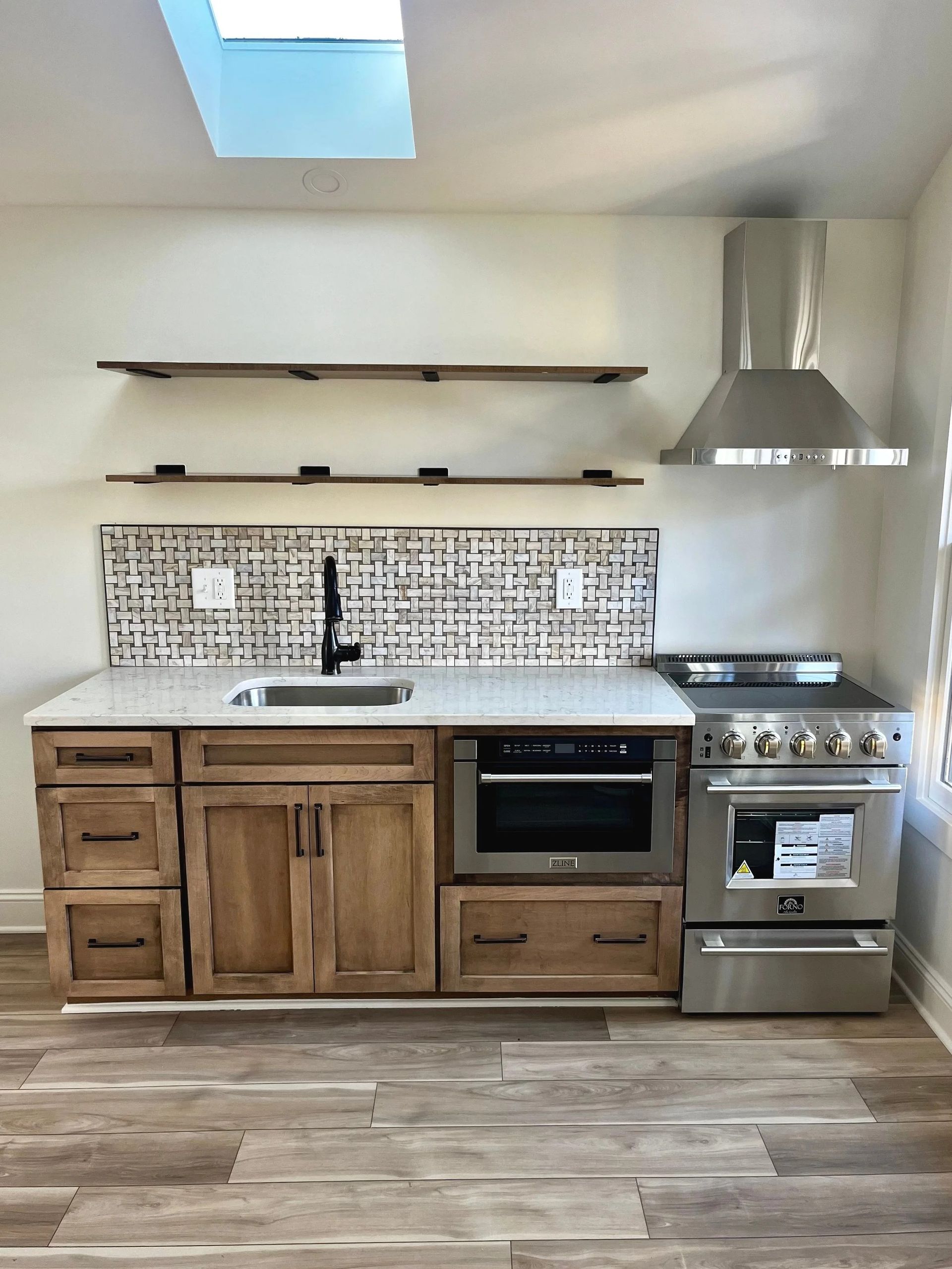 Modern kitchen with wood cabinets, patterned tile backsplash, stainless stove, sink, and floating shelves