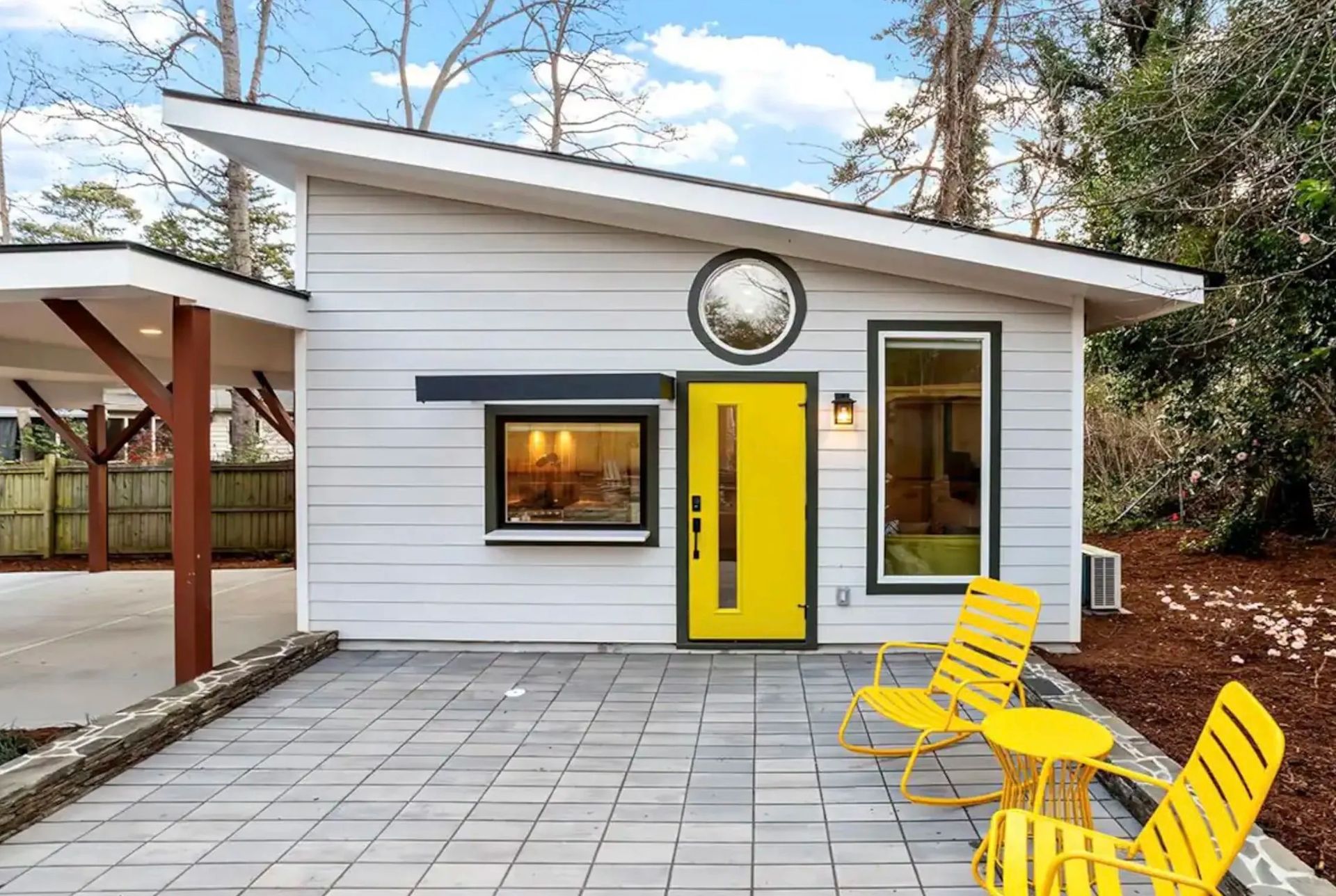 Small white house with bright yellow door and chairs on a paved patio