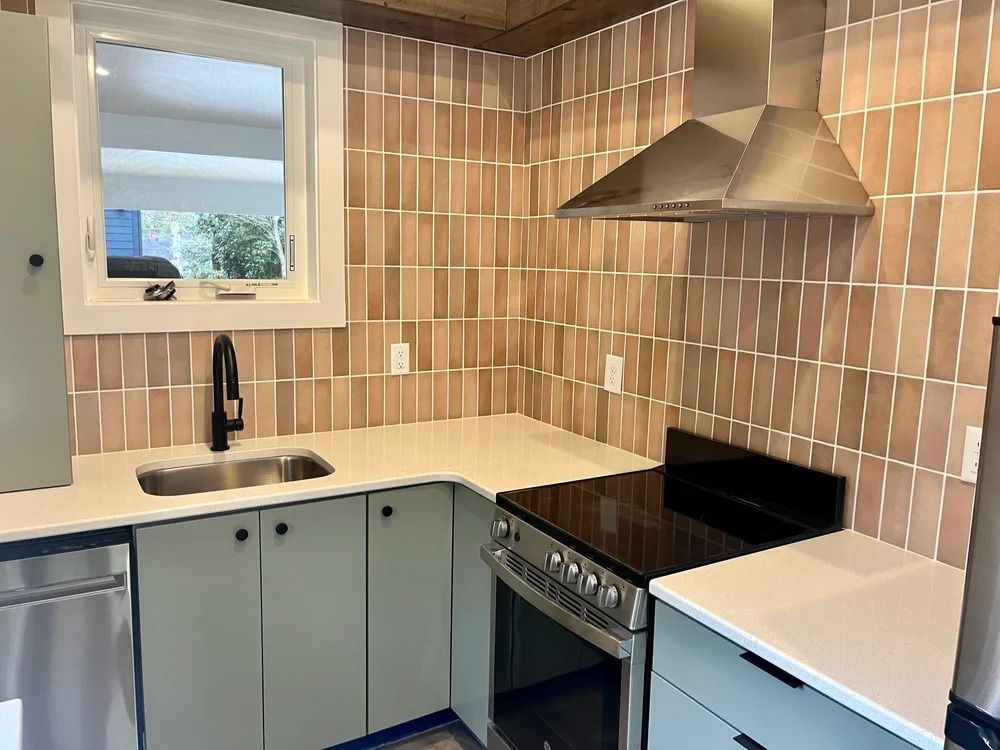 Modern kitchen with tan tile backsplash, black stove, white countertops, sink, and window above the sink