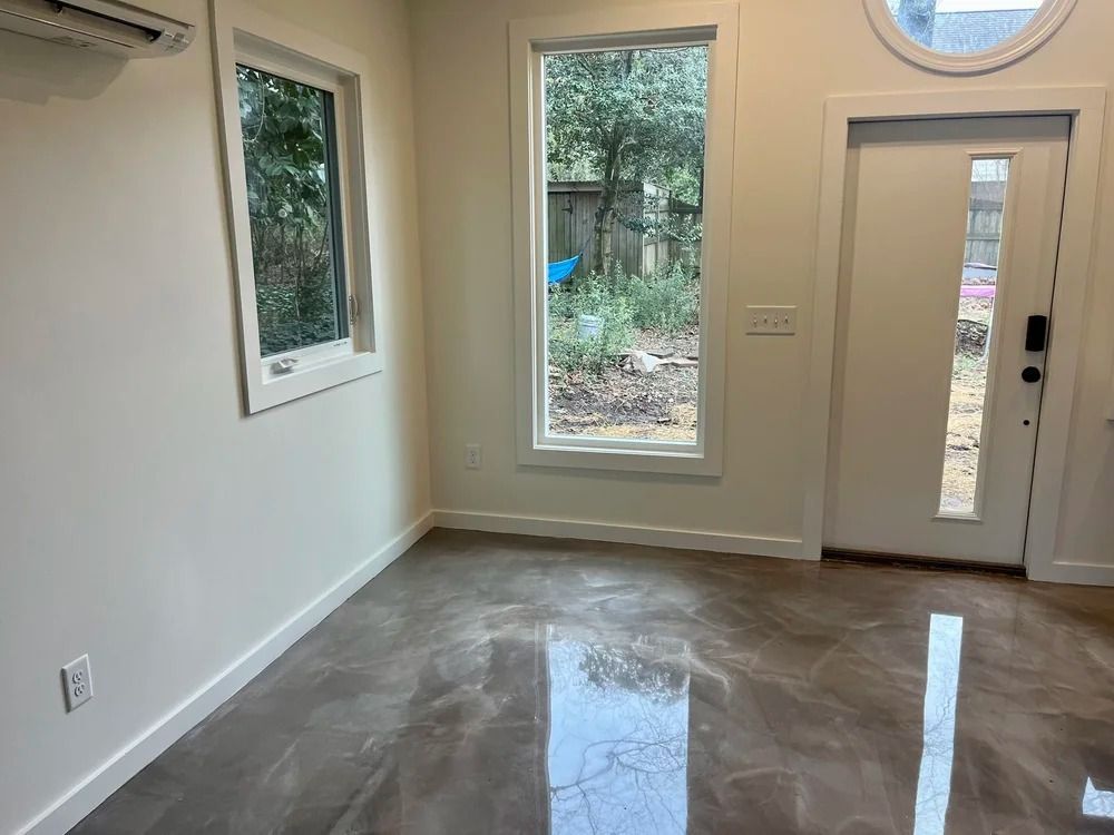 Empty modern room with glossy floors, white walls, and large windows beside a front door.