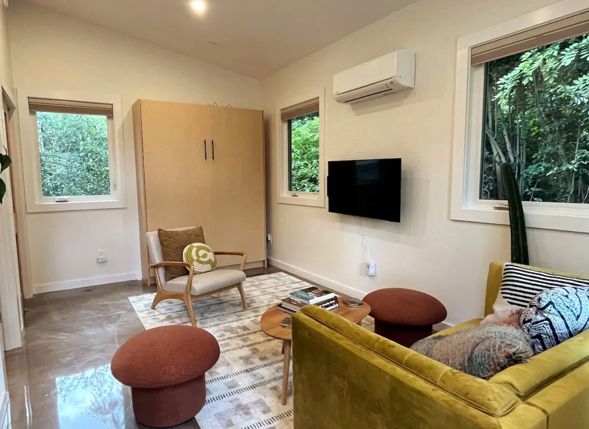 Modern living room with yellow sofa, chair, wall-mounted TV, windows, and an air conditioner