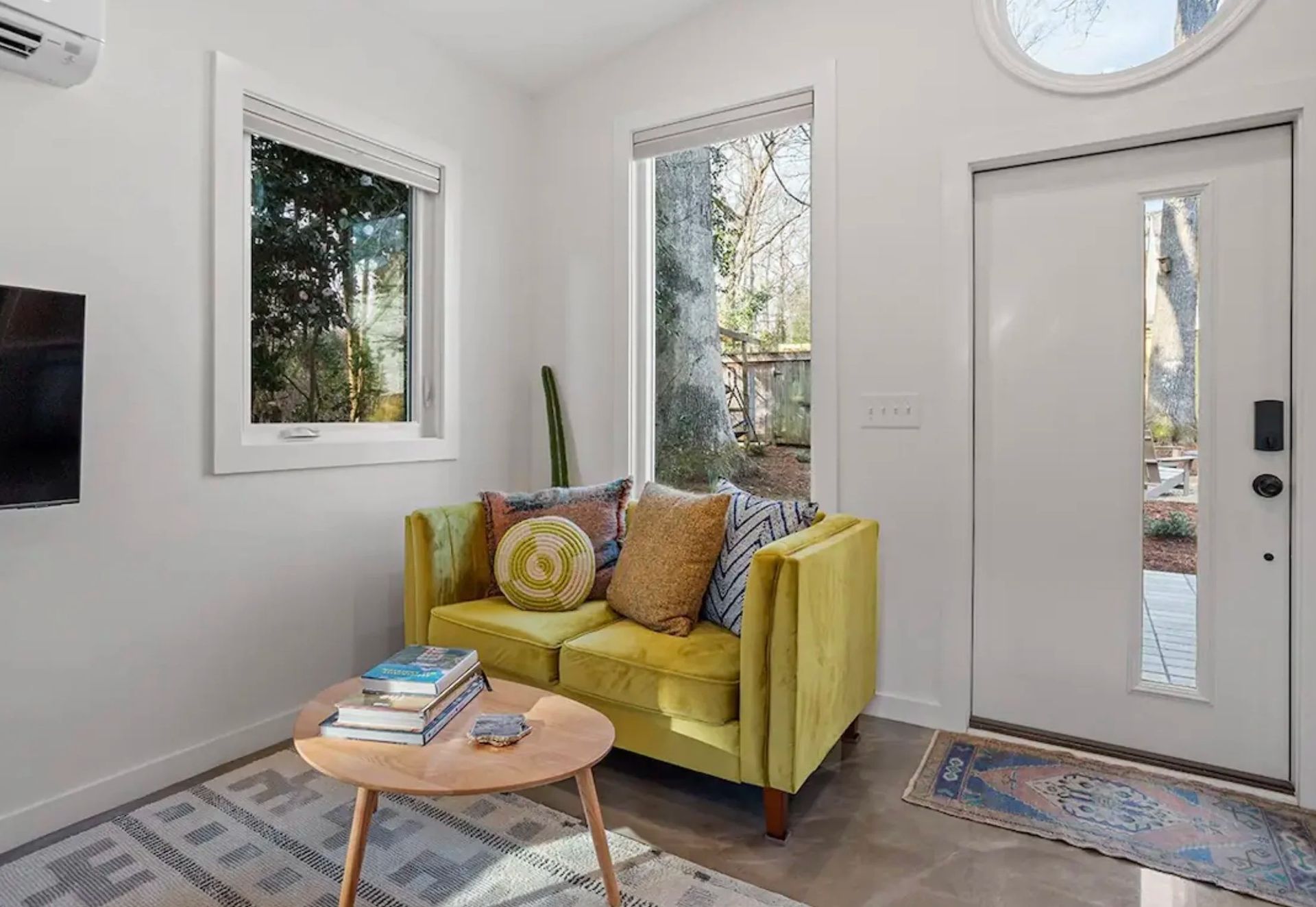 Bright living room with yellow loveseat, round coffee table, windows, and front door with sidelights