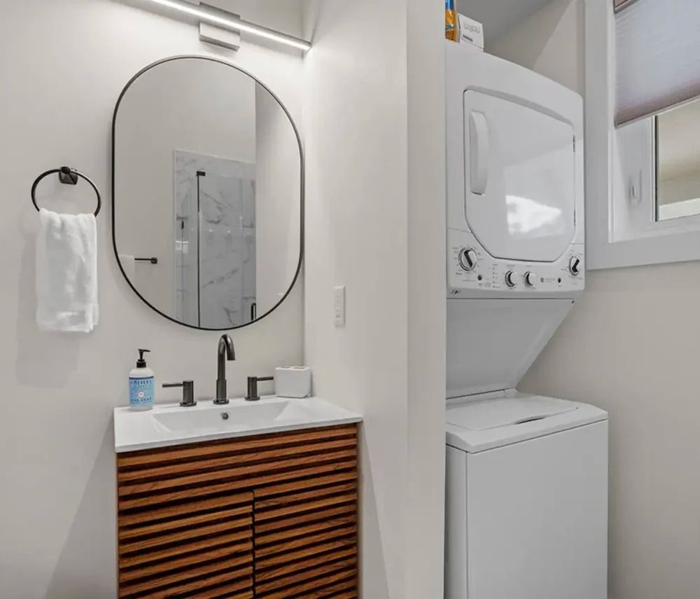 Modern bathroom vanity with round mirror and stacked washer-dryer in a white alcove