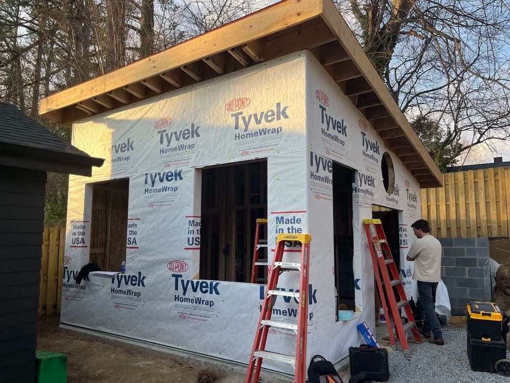 Small house under construction wrapped in Tyvek, with two workers and ladders at the front and side.