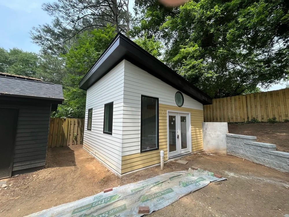 Small white backyard shed with black trim, double glass doors, and a sloped roof on a fenced lot.