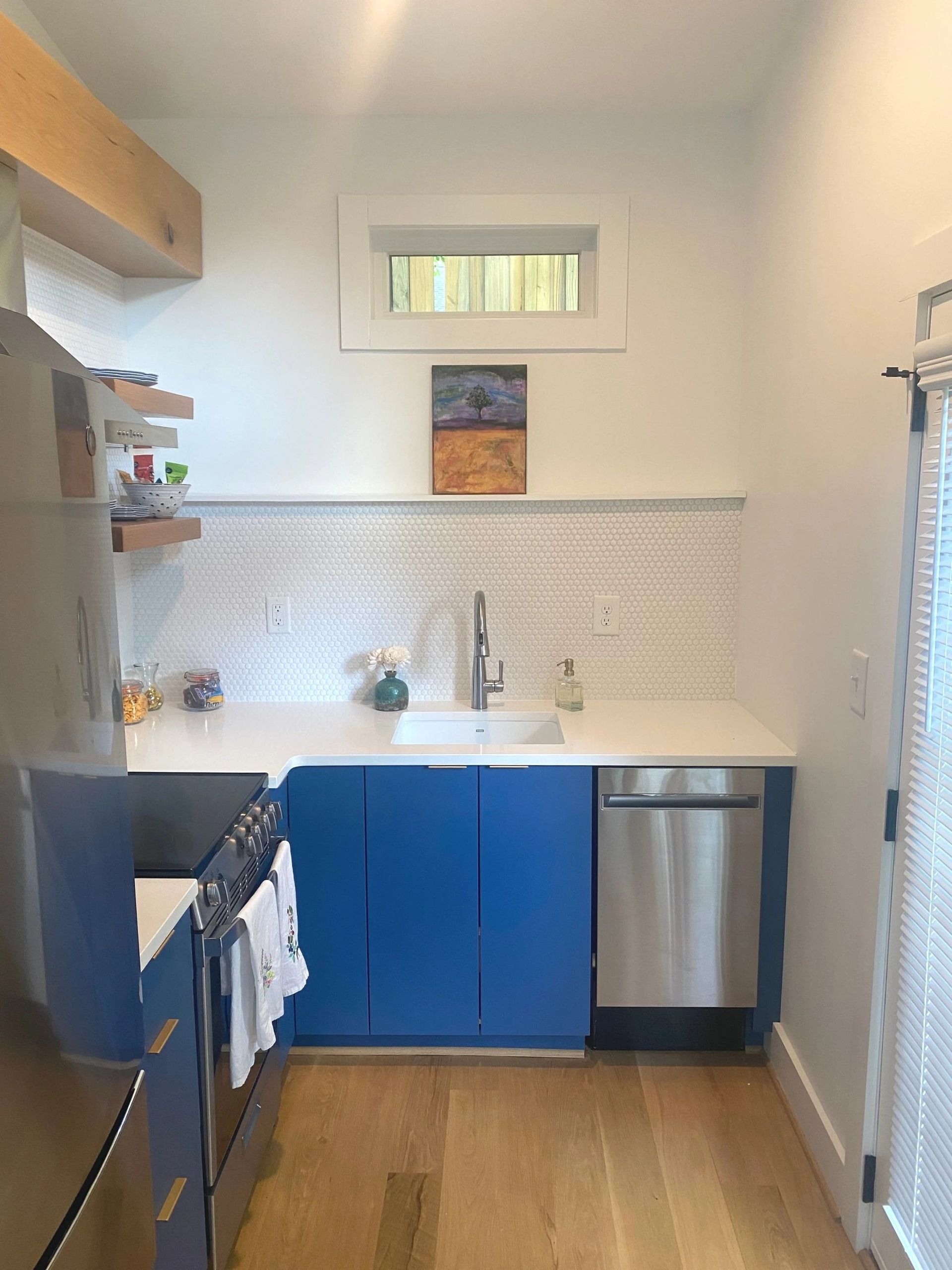 Small kitchen with blue cabinets, white tile backsplash, stainless dishwasher, and wood floor