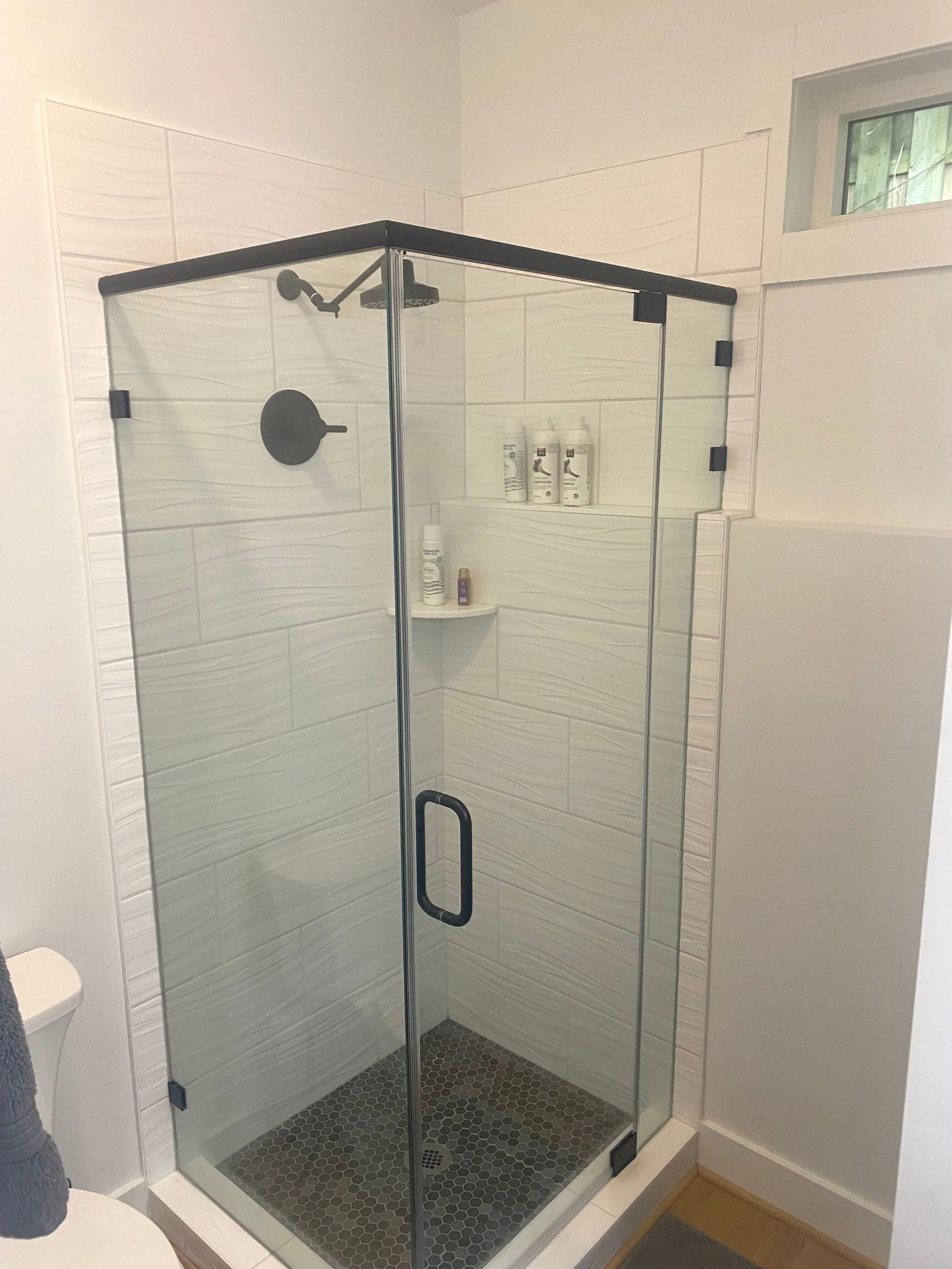 Glass walk-in shower with black-framed door and white tile walls in a bathroom