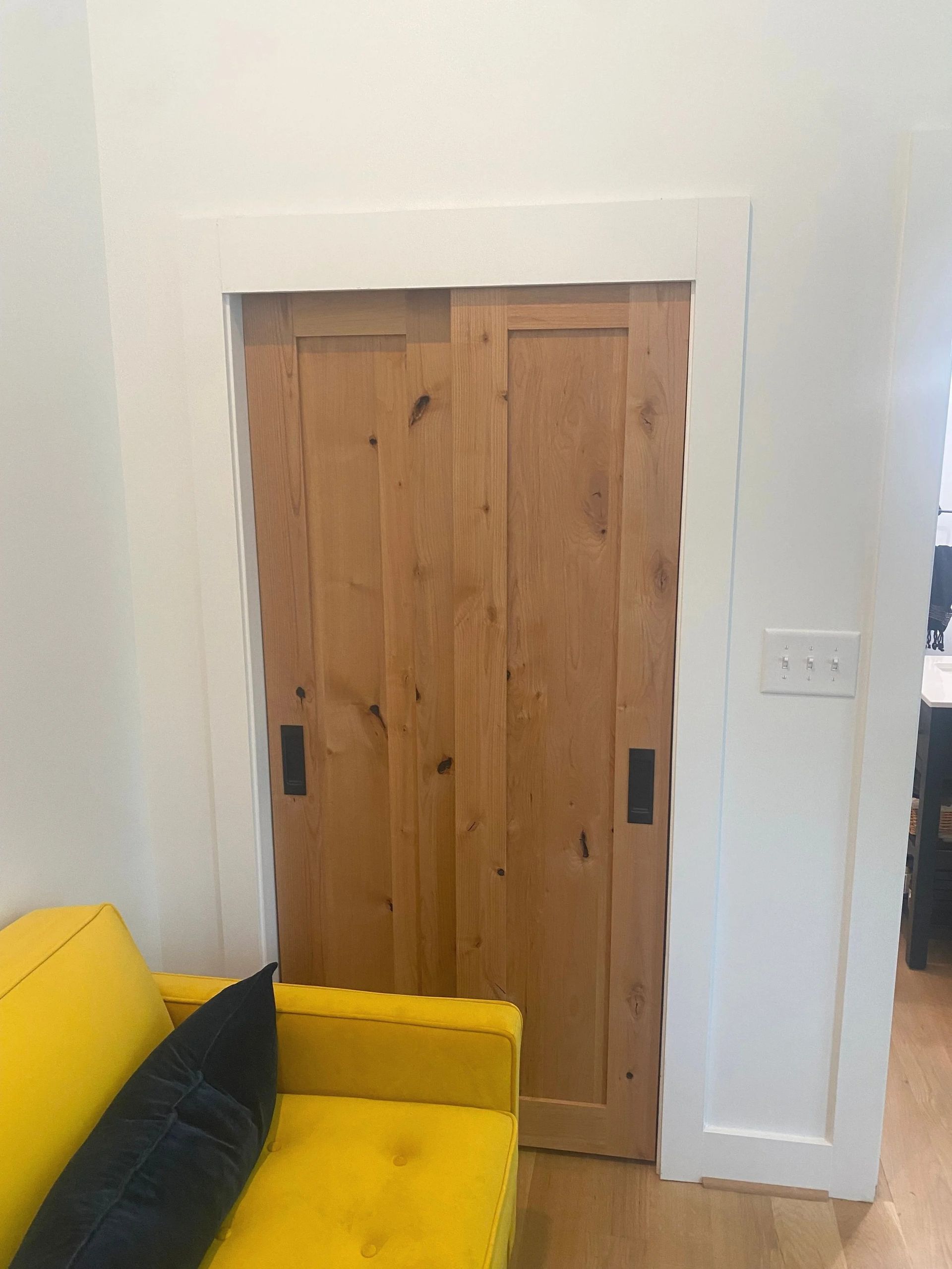 Wooden sliding door in a white room beside a yellow couch with a dark pillow