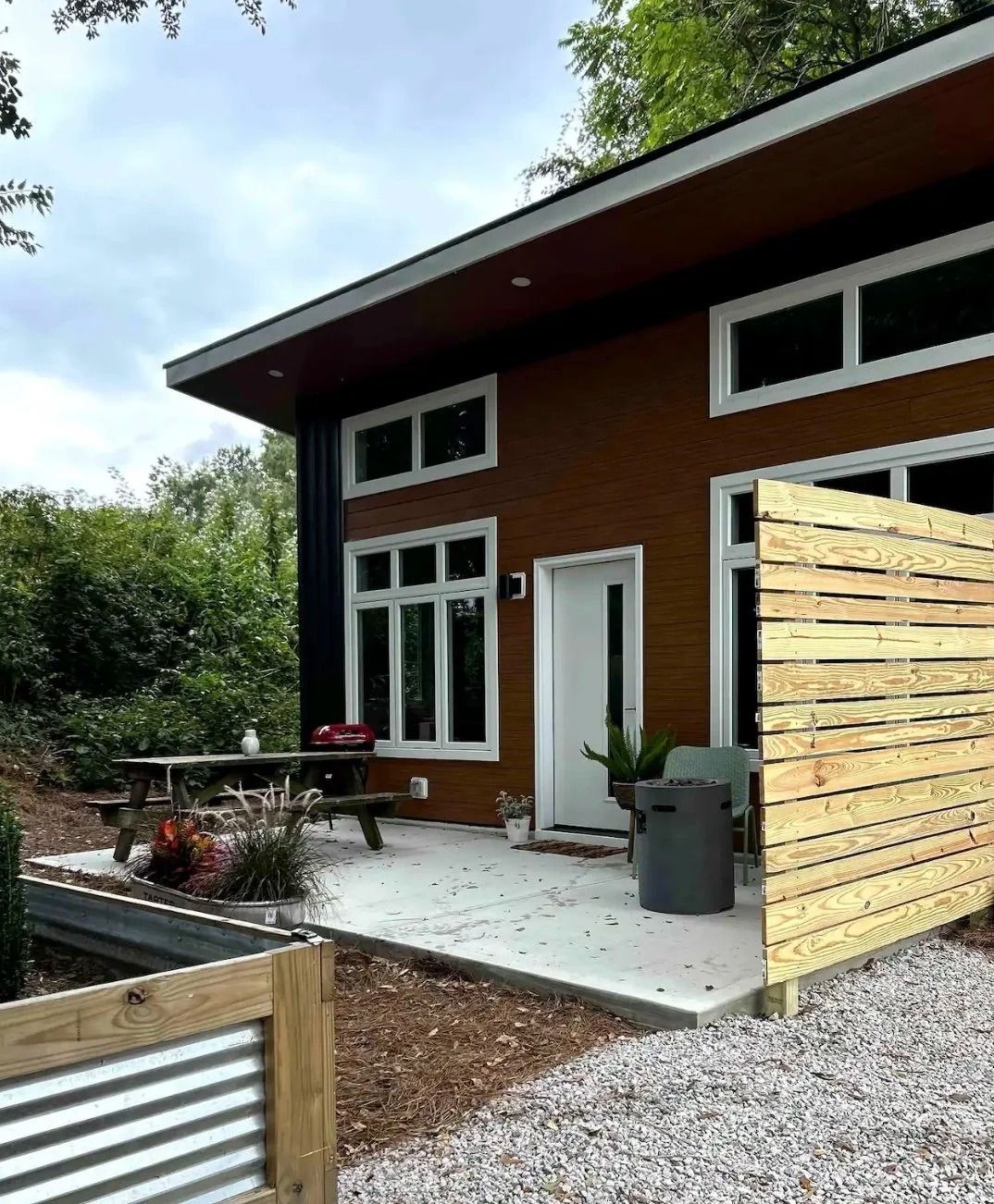 Modern brown house with patio, white doors and windows, gravel yard, and wooden privacy screen