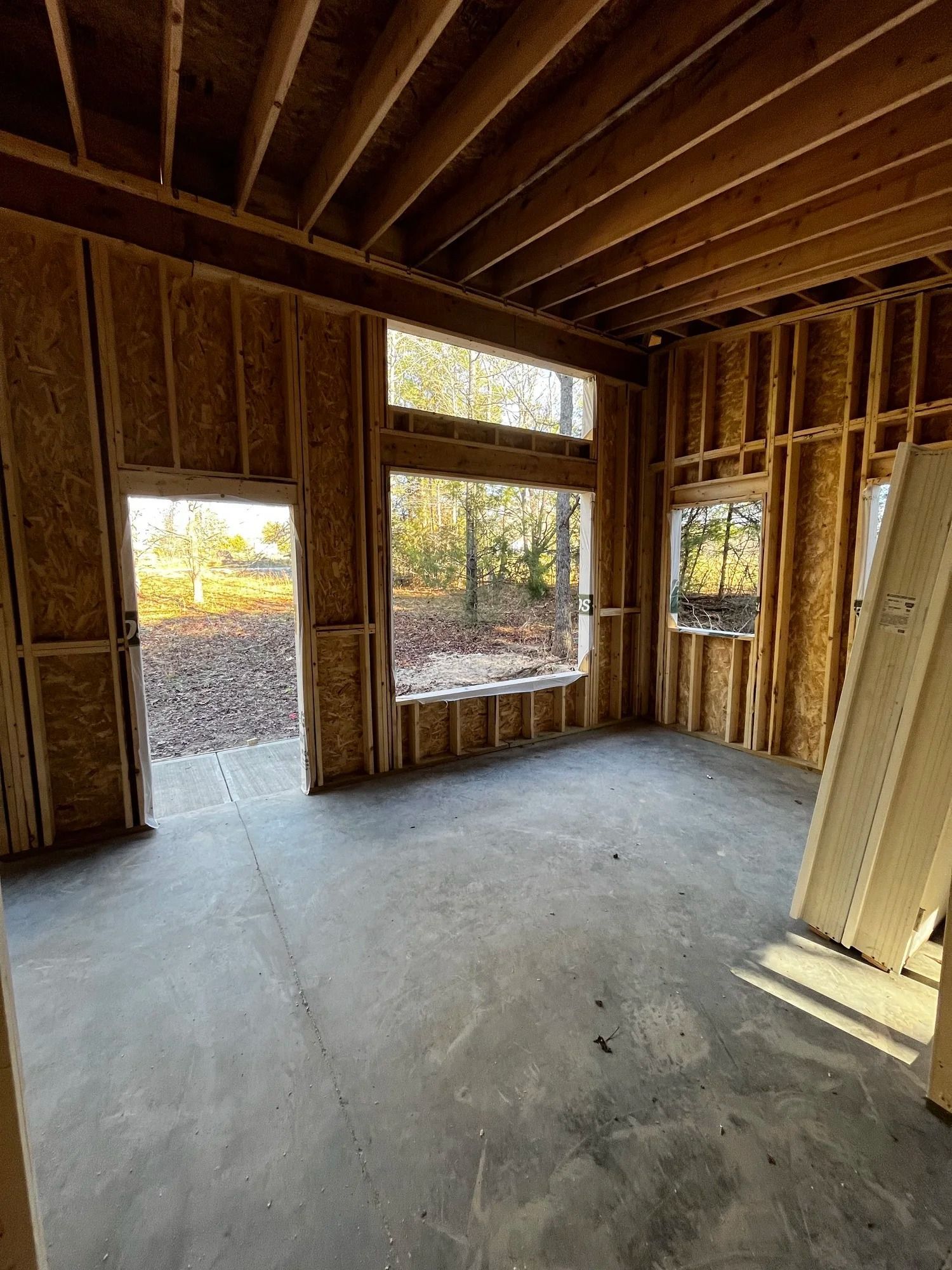 Unfinished room with exposed wood framing, concrete floor, and several window openings.