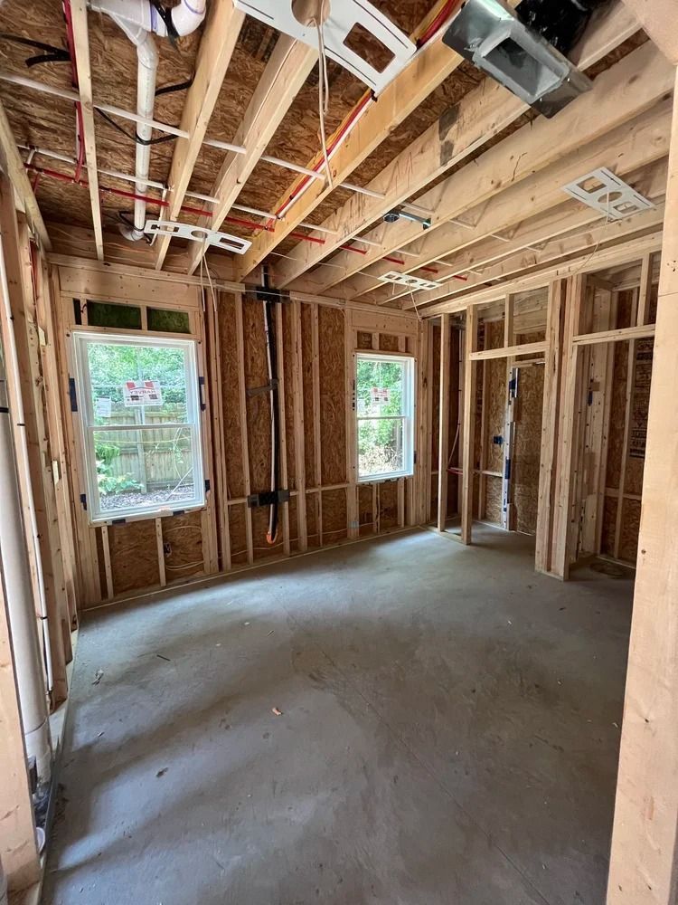 Unfinished house interior with exposed wooden framing, concrete floor, and two window openings.