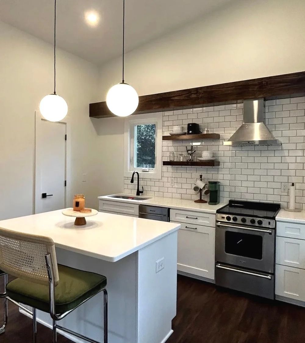 Modern kitchen with white island, pendant lights, tiled backsplash, and stainless steel stove and hood