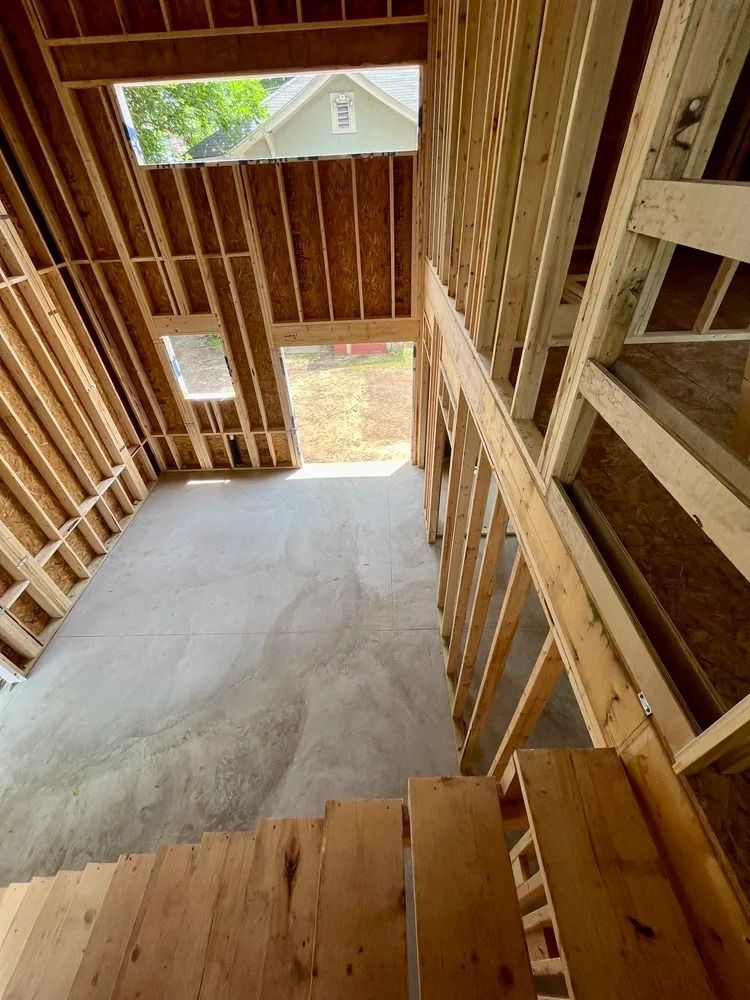 Interior of an unfinished wooden staircase and hallway under construction, with exposed framing and a concrete floor.