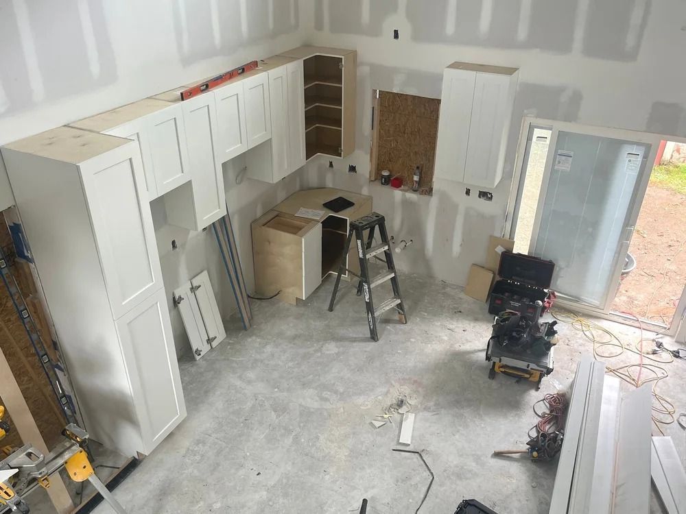 Renovation kitchen with white cabinets, tools, ladder, and unfinished drywall