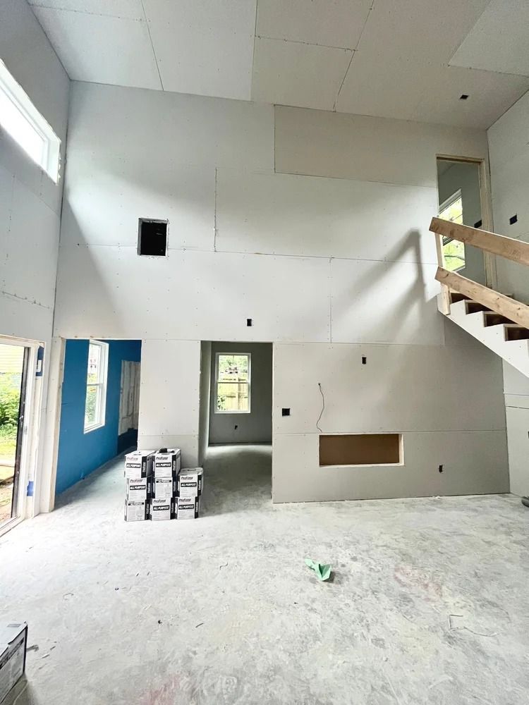 Empty unfinished room with white walls, concrete floor, stacks of boxes, and an open staircase on the right.