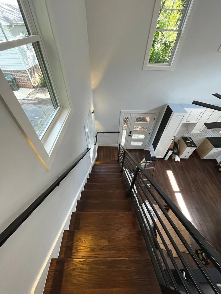 Staircase with dark wood steps, black railing, and tall windows in a bright modern interior