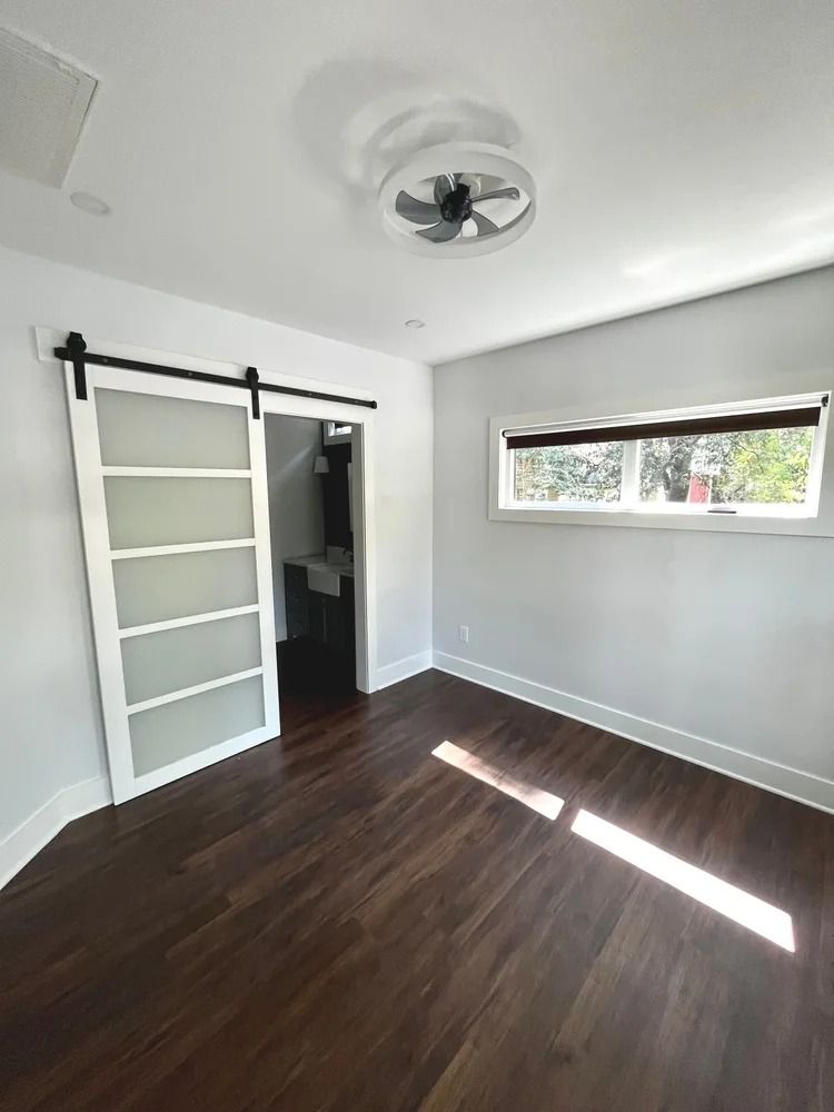Empty modern room with white walls, dark wood floor, sliding barn door, and narrow horizontal window.