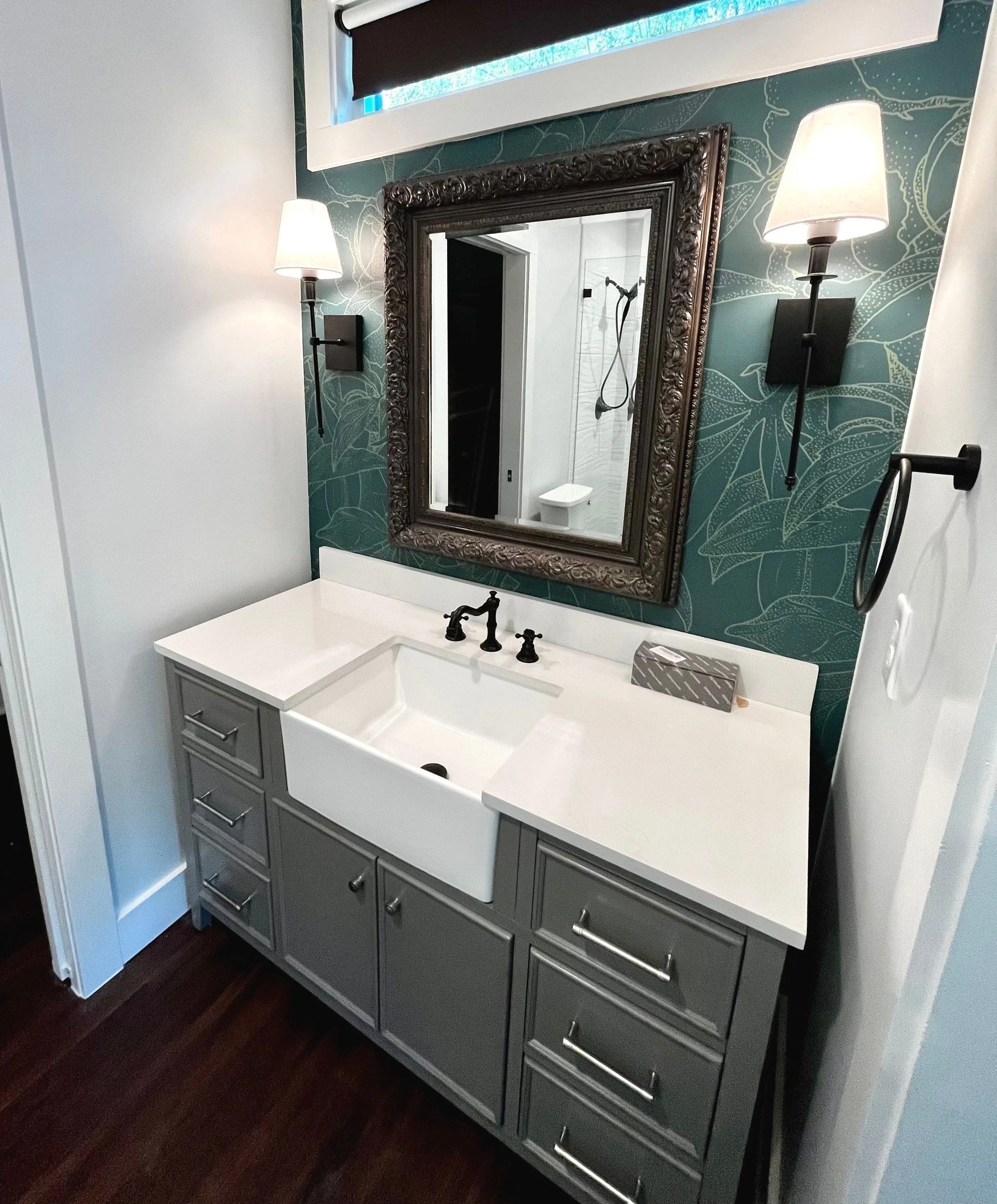 Modern bathroom vanity with white sink, gray cabinets, teal textured wall, mirror, and wall sconces