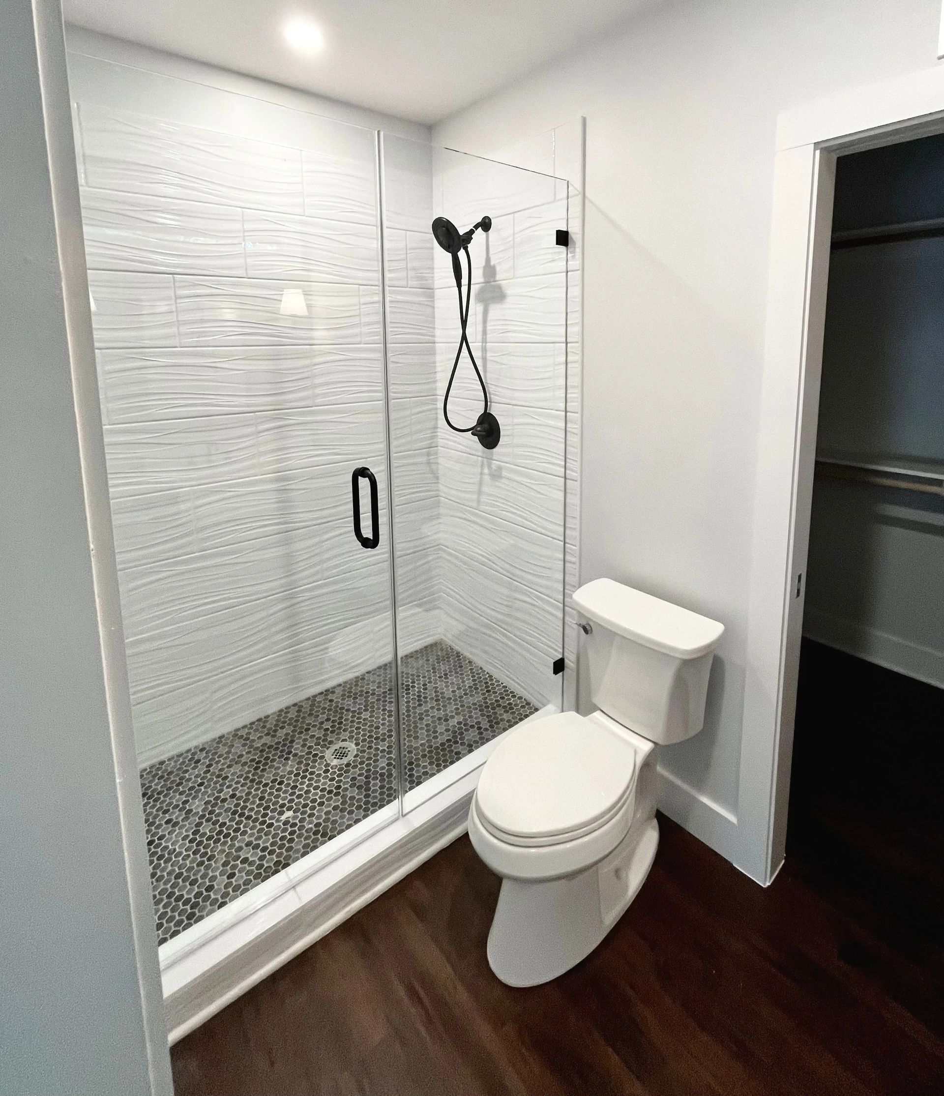 Small bathroom with glass shower, white toilet, and dark wood floor.