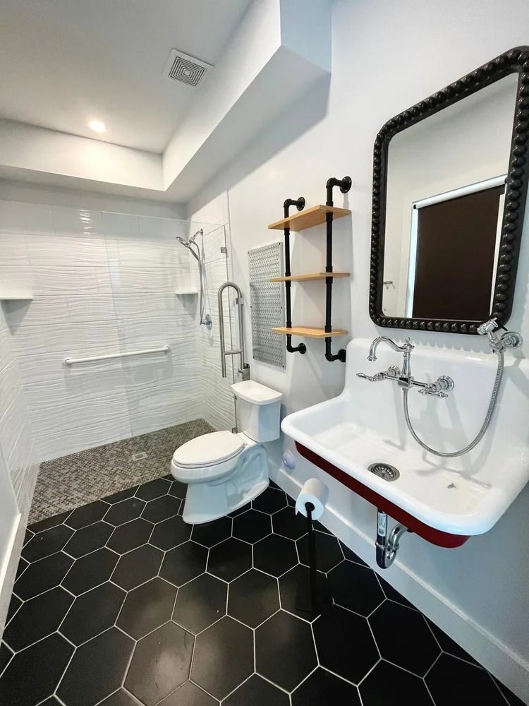 Modern bathroom with black hex tile floor, white walls, toilet, sink, mirror, and shower stall