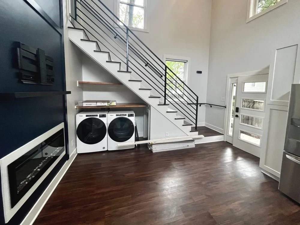 Modern laundry room with white staircase, dark wood floors, washer-dryer, and wall-mounted fireplace