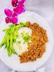 A white plate topped with meat , rice and green beans next to a purple flower.