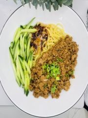 A white plate topped with noodles , meat and cucumber.