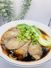 A close up of a bowl of soup with meat and vegetables on a table.